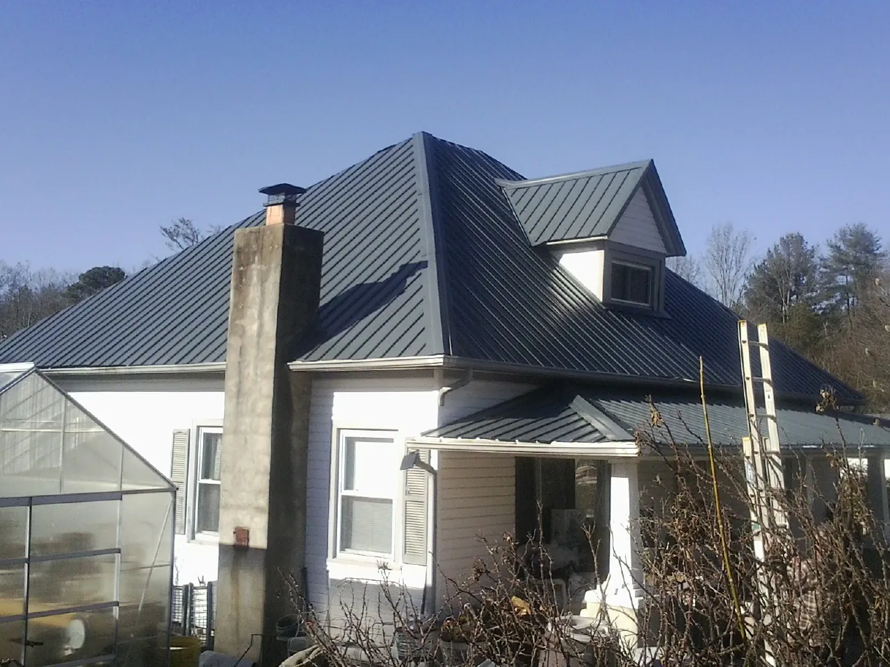 Dark blue standing seam metal roof on a white farmhouse with dormer — Slate & Tile Roof Repair by Roofing Brothers in Evans