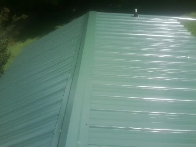 New green metal panels meeting at the ridge of a roof — Flat Roof Repair work by our crew in Evans