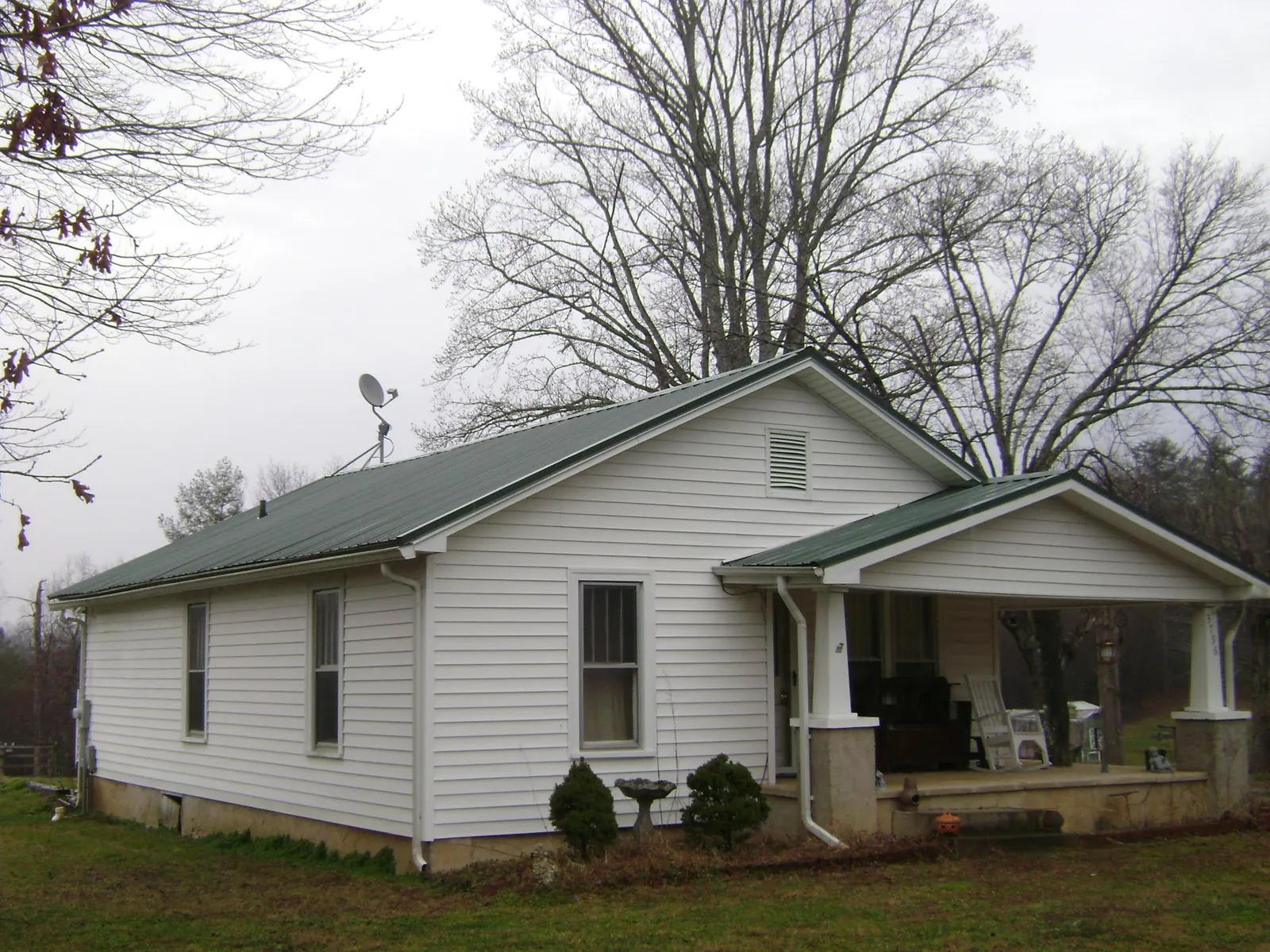 Green metal roof on a white bungalow with a side porch in Evans