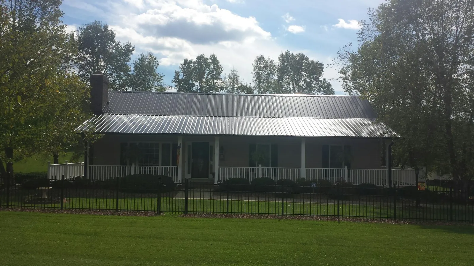 Gray metal roof on a brick ranch with a full width front porch — Gutter Guard Installation work by our crew in Evans